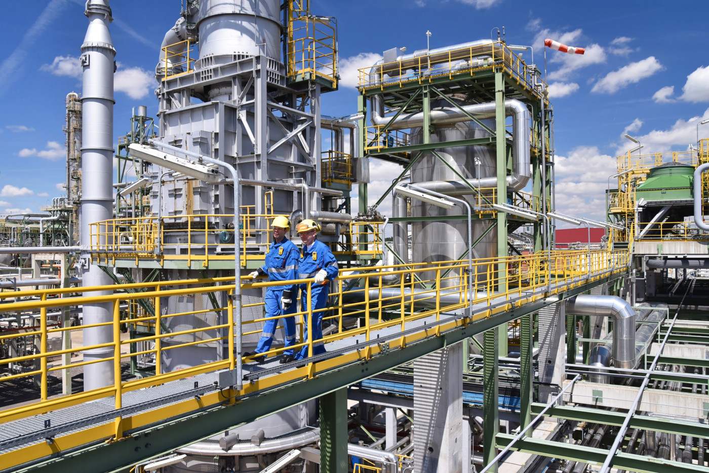 Chemiefabrik, zwei Arbeiter in Arbeitsbekleidung und mit Helm begehen die Anlage