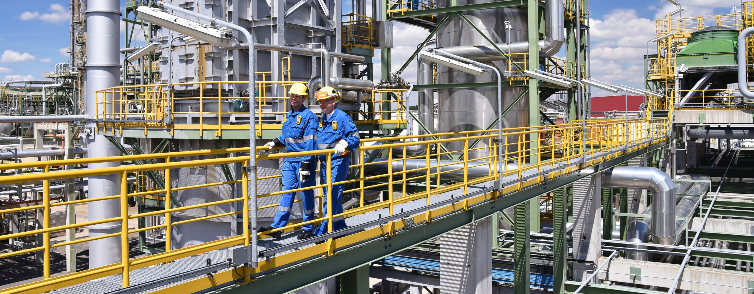 Chemiefabrik, zwei Arbeiter in Arbeitsbekleidung und mit Helm begehen die Anlage
