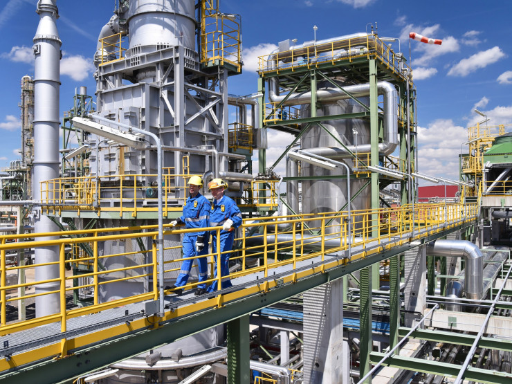 Chemiefabrik, zwei Arbeiter in Arbeitsbekleidung und mit Helm begehen die Anlage